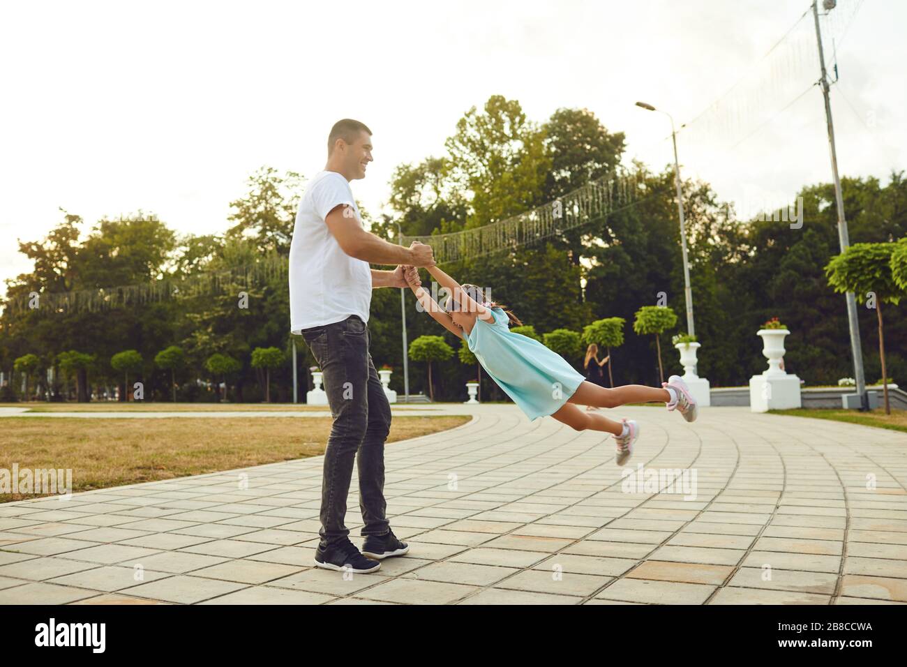 Vater und Mutter, die Spaß haben, werfen eine Tochter auf die Straße. Glücklich lächelnde Familie, die auf der Straße spazieren geht. Stockfoto