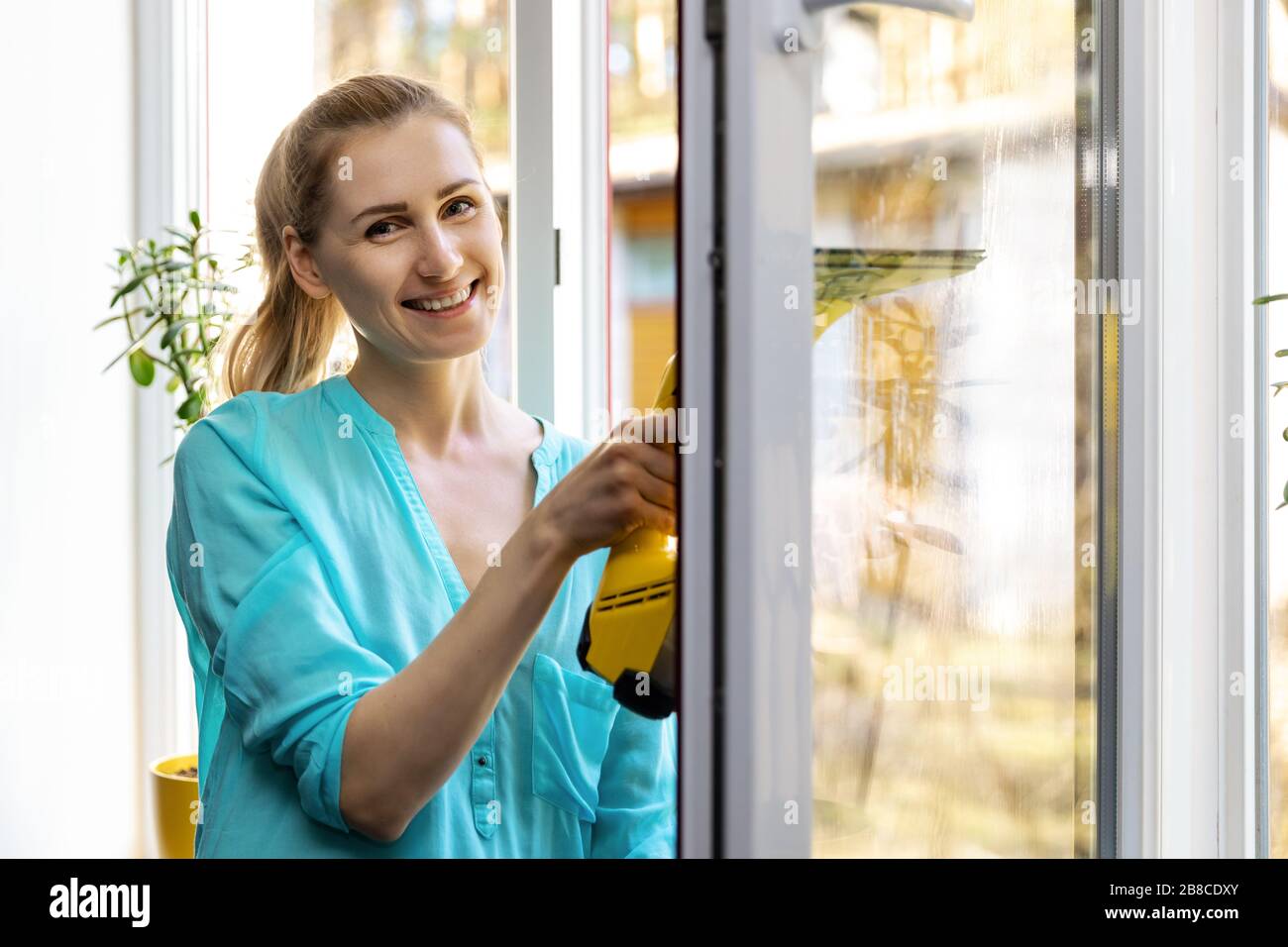 Frau reinigen Fensterglas mit Staubsauger zu Hause Stockfoto