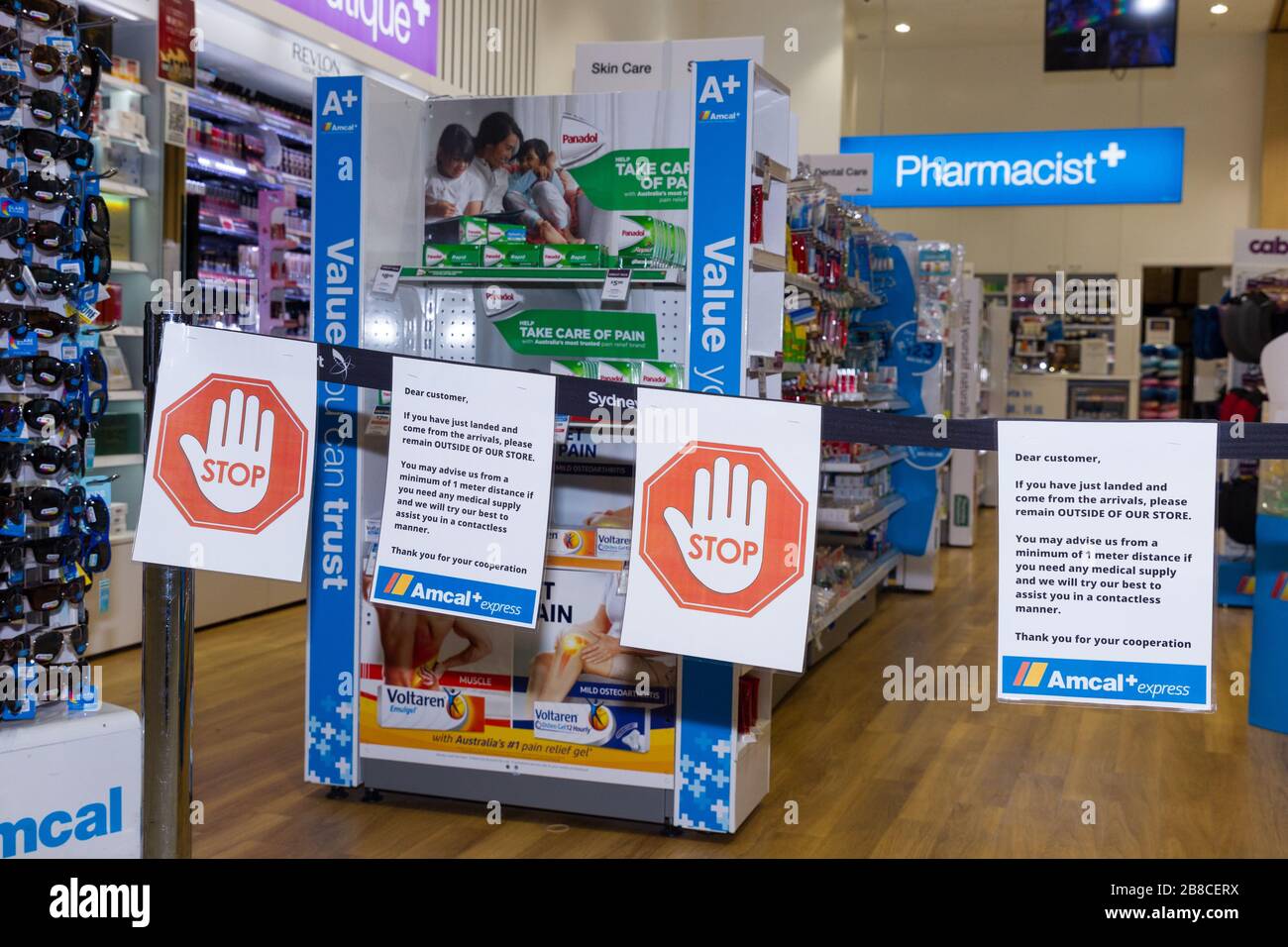 Coronavirus Warnschilder und Sicherheitsbarrieren in einer Amcal Apotheke am internationalen Abflugterminal des Flughafens Sydney (Kingsford Smith) in Australien. Der Chemiker hatte die Barriere und Warnungen am Ladeneingang platziert, um Flugpassagiere, die gerade nach Australien gekommen waren, zu bitten, sich an "soziale Distanzierungsregeln" zu halten, um das Risiko einer Verbreitung des Coronavirus zu verringern. Stockfoto