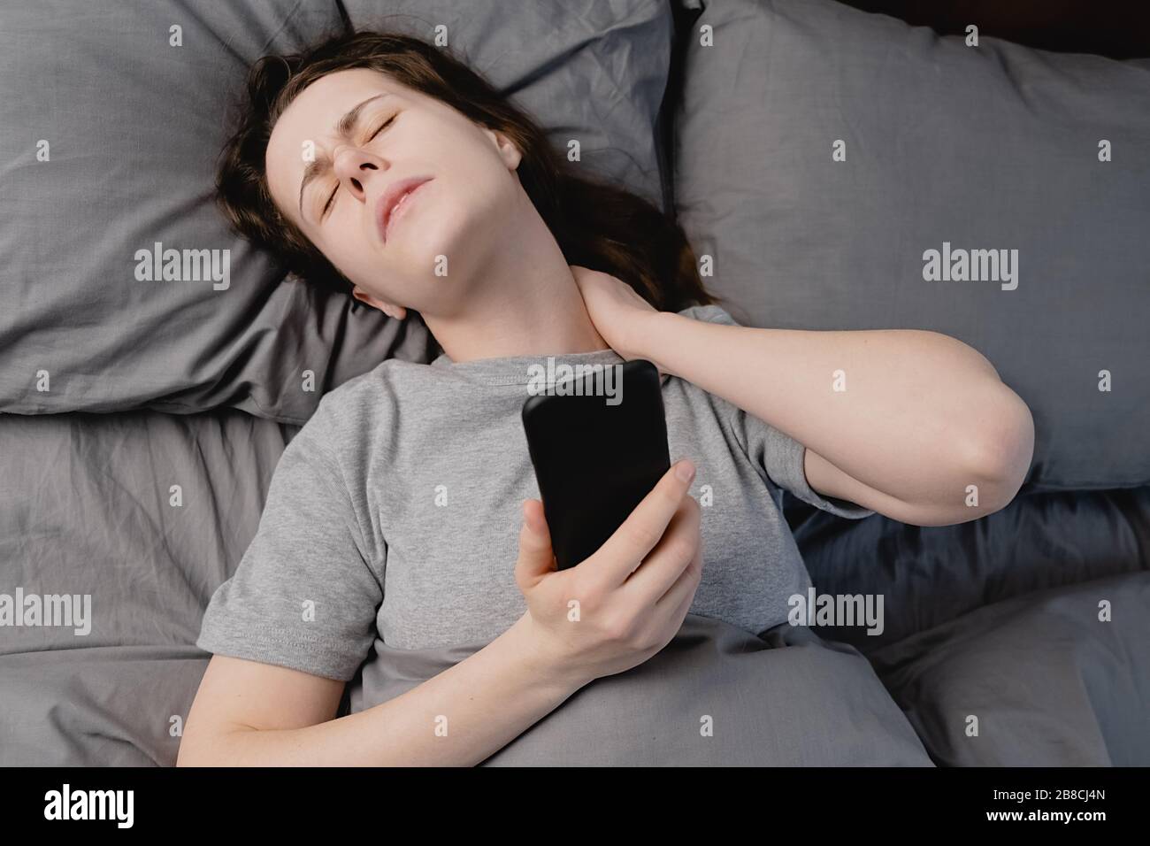 Fibromyalgie-Konzept. Draufsicht auf unglückliche junge Frau, die morgens  im Bett liegt, spürt Schmerzen im Nacken nach dem Schlaf, massiert  angespannte Nackenmuskeln Stockfotografie - Alamy