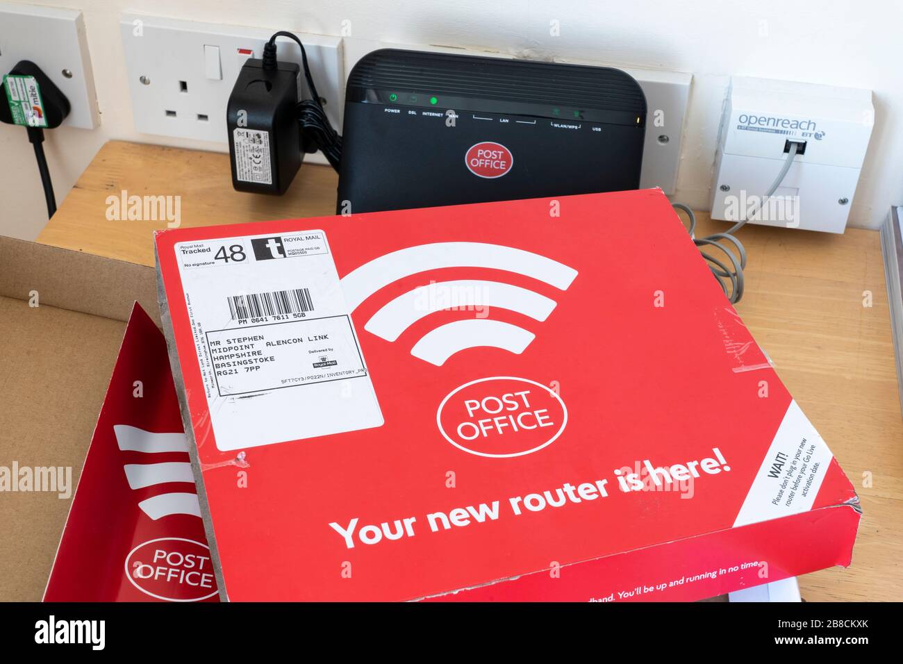 Ein Breitband-Internet-Router, der an eine Steckdose angeschlossen ist, die von der Post - einem Internet-Anbieter - an einen Privatbenutzer in Großbritannien gesendet wird Stockfoto