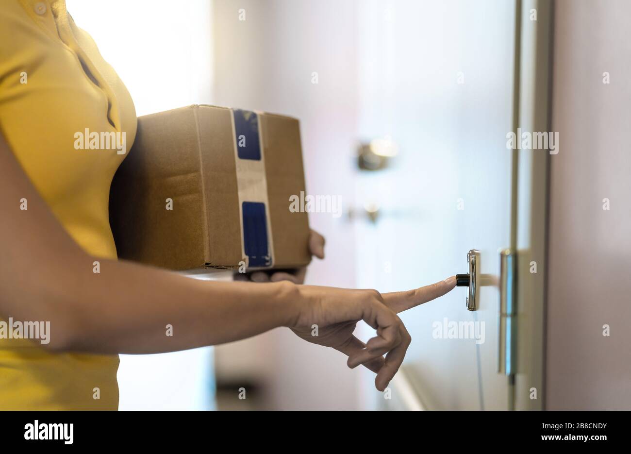 Lieferperson, die das Paket an die Haustür liefert. Versandservice. Frau läutet Türklingel. Weiblicher Kurier, der die Kartonbox im Gebäude arbeitet und hält. Stockfoto