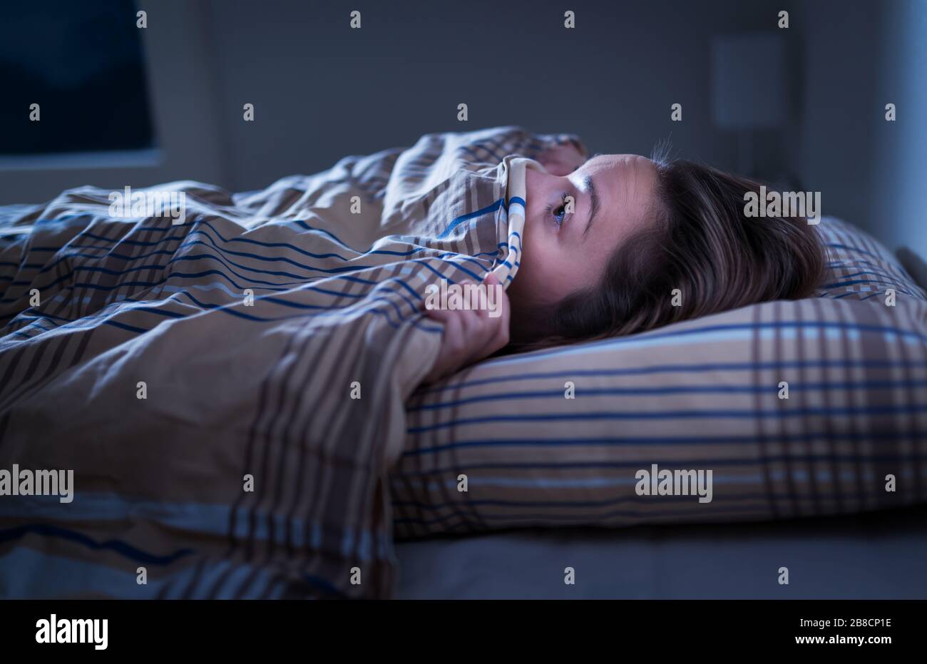 Erschrockene Frau versteckt sich unter Decke. Angst vor der Dunkelheit. Schlafen nach Alptraum oder schlechtem Traum nicht möglich. Mitten in der Nacht im Schlafzimmer wach. Stockfoto