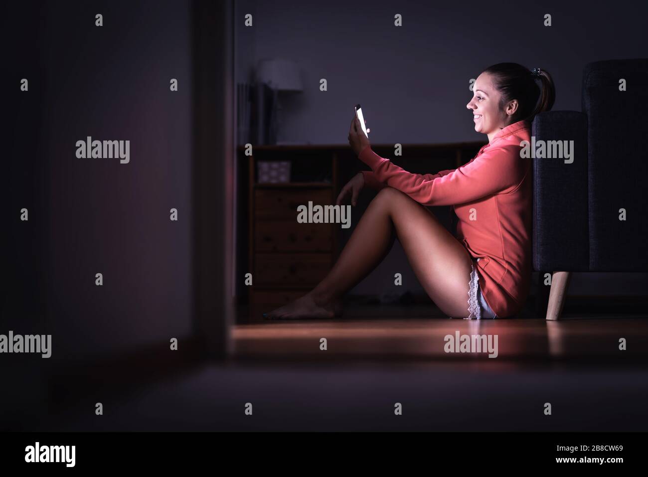 Frau liest nachts Texte mit Smartphone. Lächelnde Person mit Handy. Glückliche Dame, die datiert und flirtet. Tratsch mit Freund. Neue Beziehung. Stockfoto