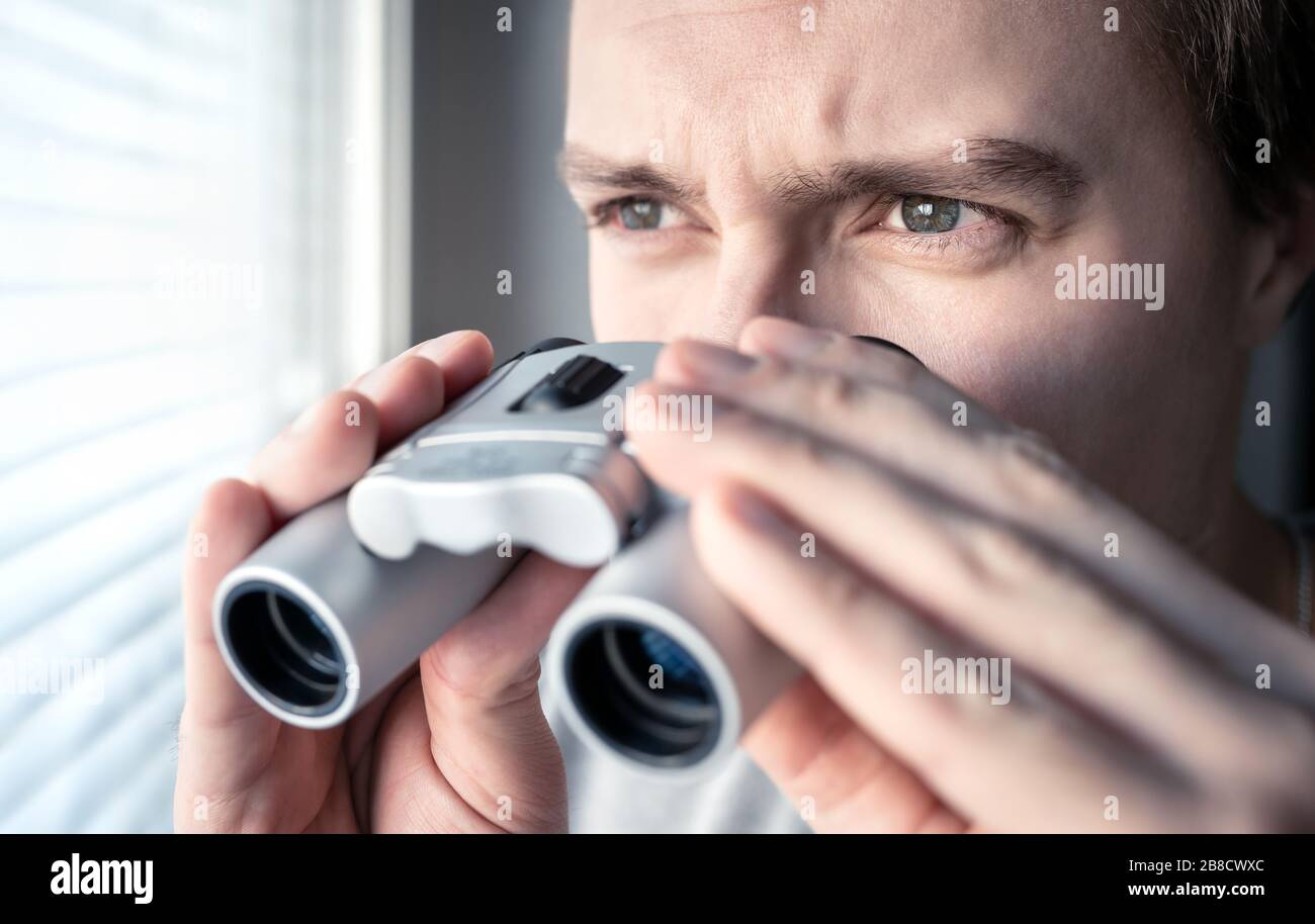 Mann mit Fernglas. Privatdetektiv, Agent oder Ermittler, der das Fenster betrachtet. Mann ausspioniert oder untersucht. Privatsphäre, Überwachung oder Spionage. Stockfoto
