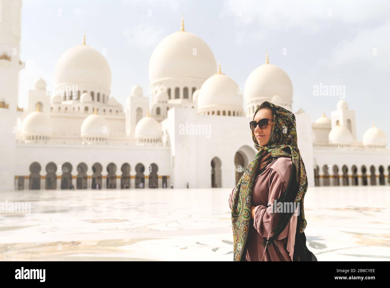 Glückliche Frau in der Scheich Zayed Grand Moschee. Touristin mit Kopftuch und Kleid in Adu Dhabi. Dame, die in einem traditionellen muslimischen Gebäude spazieren geht. Stockfoto