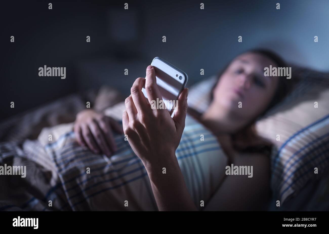 Traurige Frau, die nachts im Bett auf das Smartphone blickt. Anruf von unbekanntem Anrufer. Schlaflose Person, die unter Stress oder Schlaflosigkeit leidet. Stockfoto
