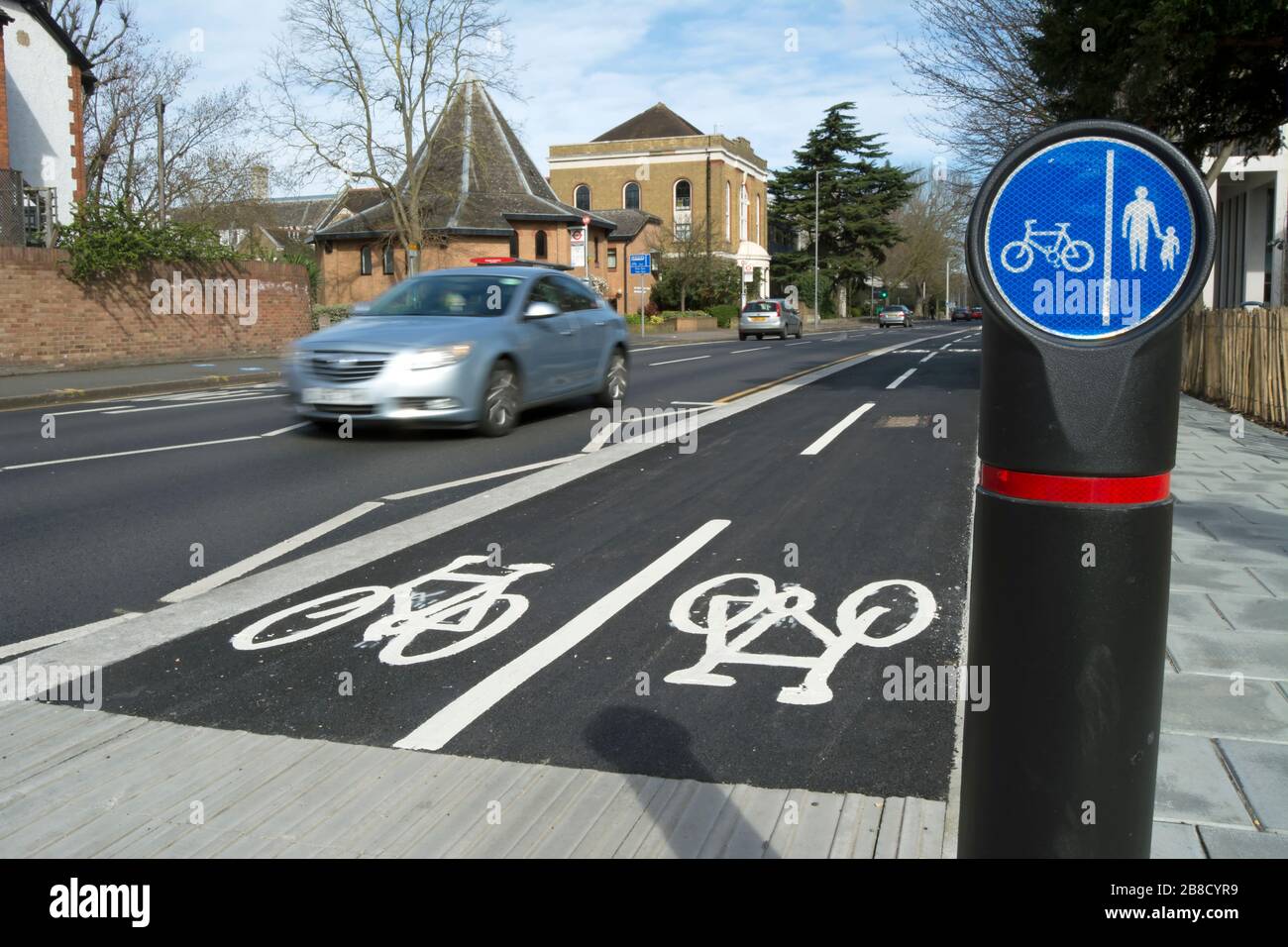 Radweg in kingston upon thames, surrey, england, mit vorbeifahrenden Autos in verschwommener Bewegung und separaten Spuren für Fußgänger und Radfahrer Schild Stockfoto