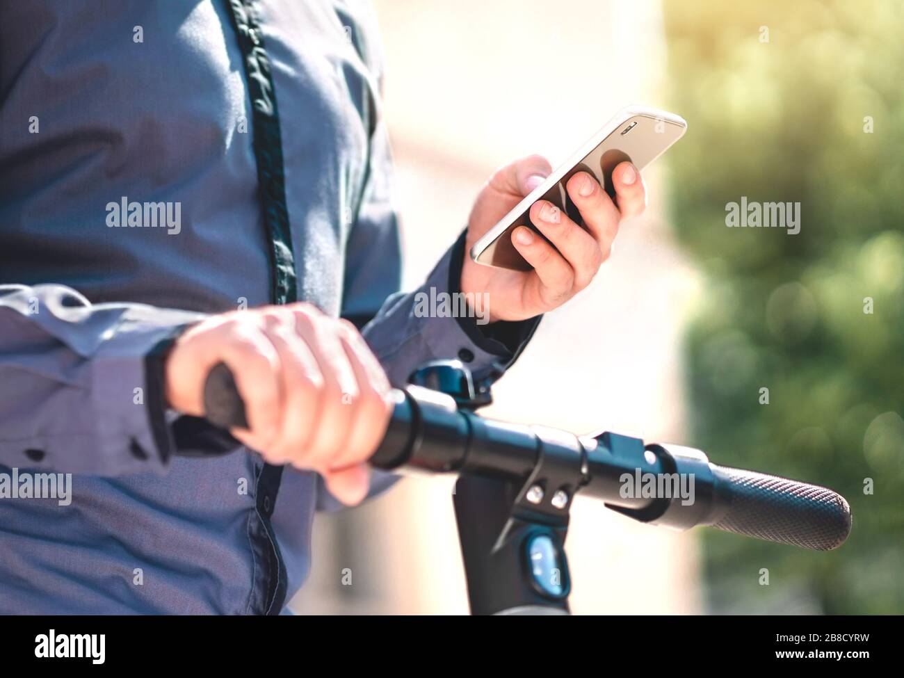 Elektrokick Roller Verleih App im Telefon. Mann, der ein E-Fahrzeug zum Pendeln mit dem Smartphone mietet. Mobile Anwendung für den Ökostrom. Stockfoto