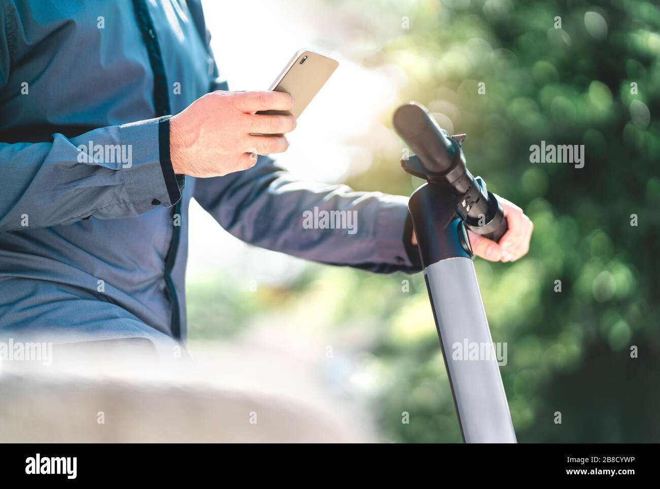 Geschäftsmann mietet elektrischen Kickroller mit Smartphone im Stadtpark. Hiphster man nutzt den Mobilfunk-Verleih in der städtischen Straße. E Fahrzeug. Stockfoto