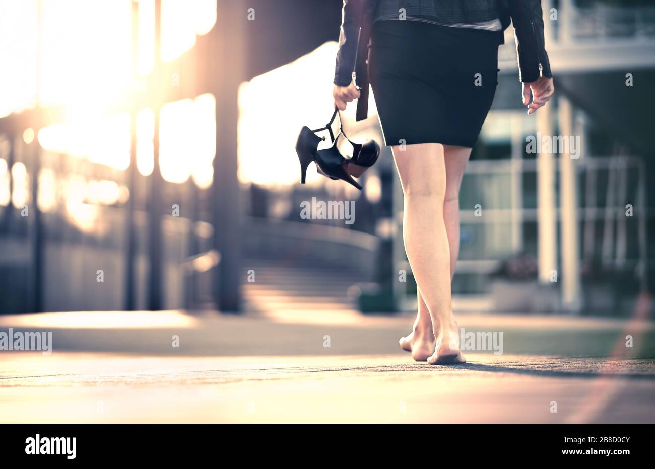 Frau hält High Heels in der Hand und geht von Party barfuß nach Hause. Geschäftsfrau nahm unbequeme Schuhe ab. Dame mit Stilettos und Miniskirt. Stockfoto