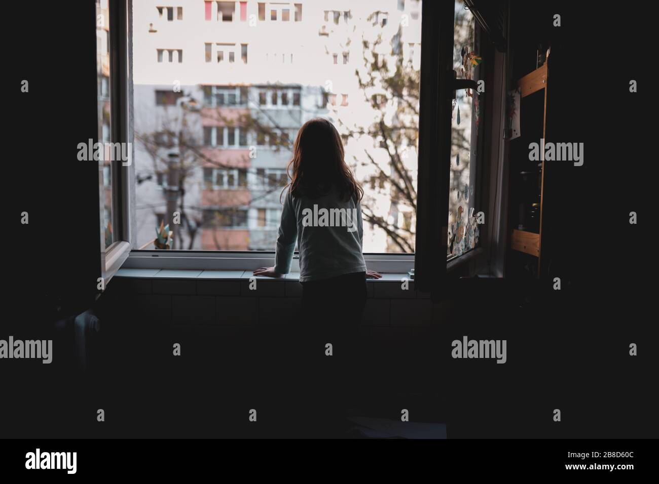 Kleines Mädchen, das während der Hausquarantäne von Covid-19 auf dem Fenster beobachtet. Stockfoto