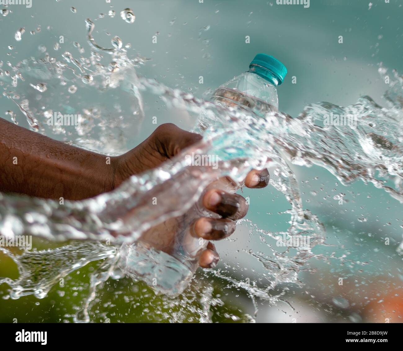 Eine Hand, die eine Wasserflasche mit Wasserspritzer und türkisfarbenem Hintergrund hält Stockfoto