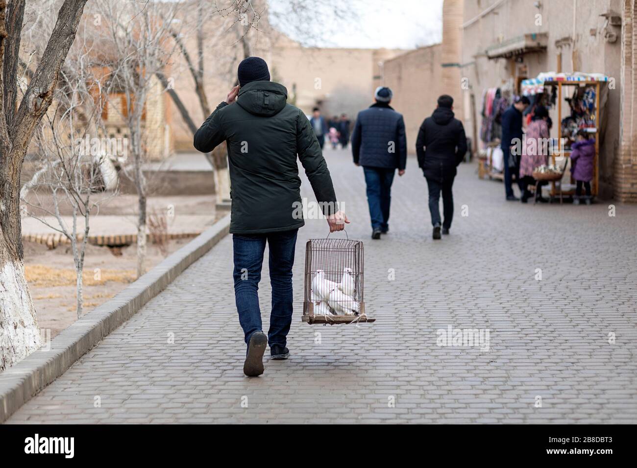 Mann, der einen Taubenkäfig zum Verkauf auf der Straße in der Altstadt von Chiwa, usbekistan, trägt Stockfoto