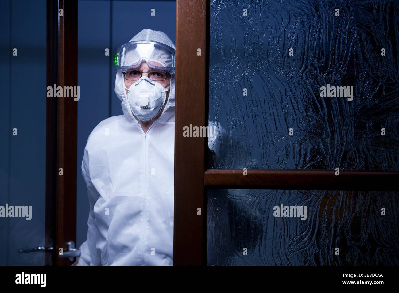 Müder Arzt, der die Kamera am Eingang eines Krankenhauses mit Schutzkleidung betrachtet - nachts mit dunkelblauem Hintergrund aufgenommen Stockfoto