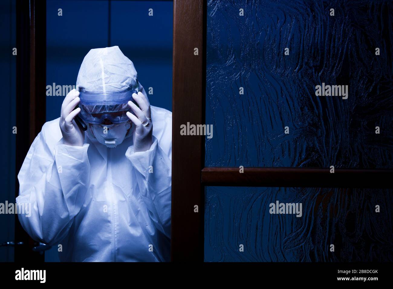Der Arzt am Eingang eines Krankenhauses legt ihm eine Schutzmaske ins Gesicht - von Nacht mit dunkelblauem Hintergrund erschossen Stockfoto
