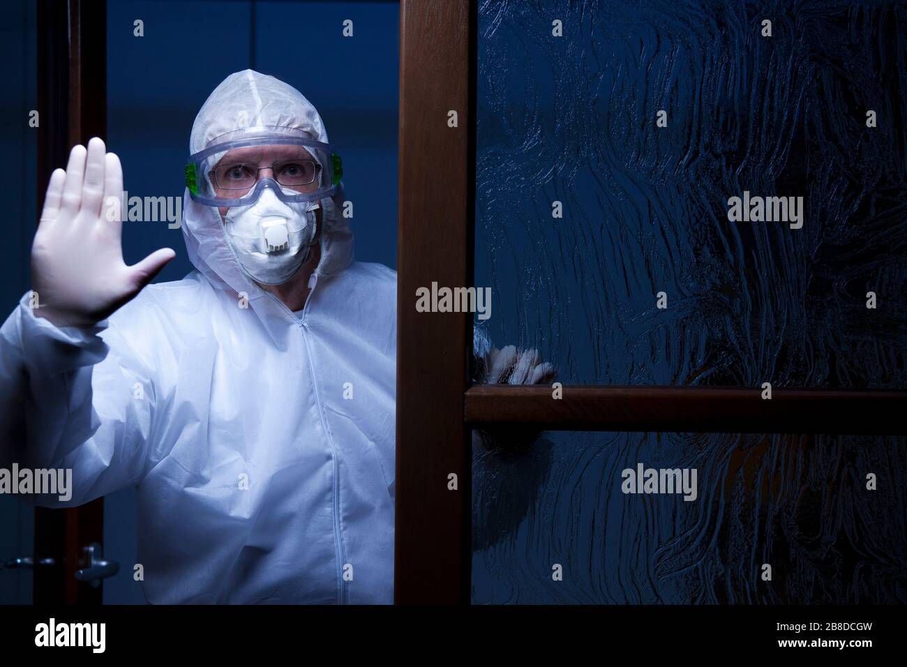 Arzt mit Schutzkleidung an einem Eingang eines Krankenhauses hält Menschen davon ab zu betreten - nachts mit dunkelblauem Hintergrund erschossen Stockfoto