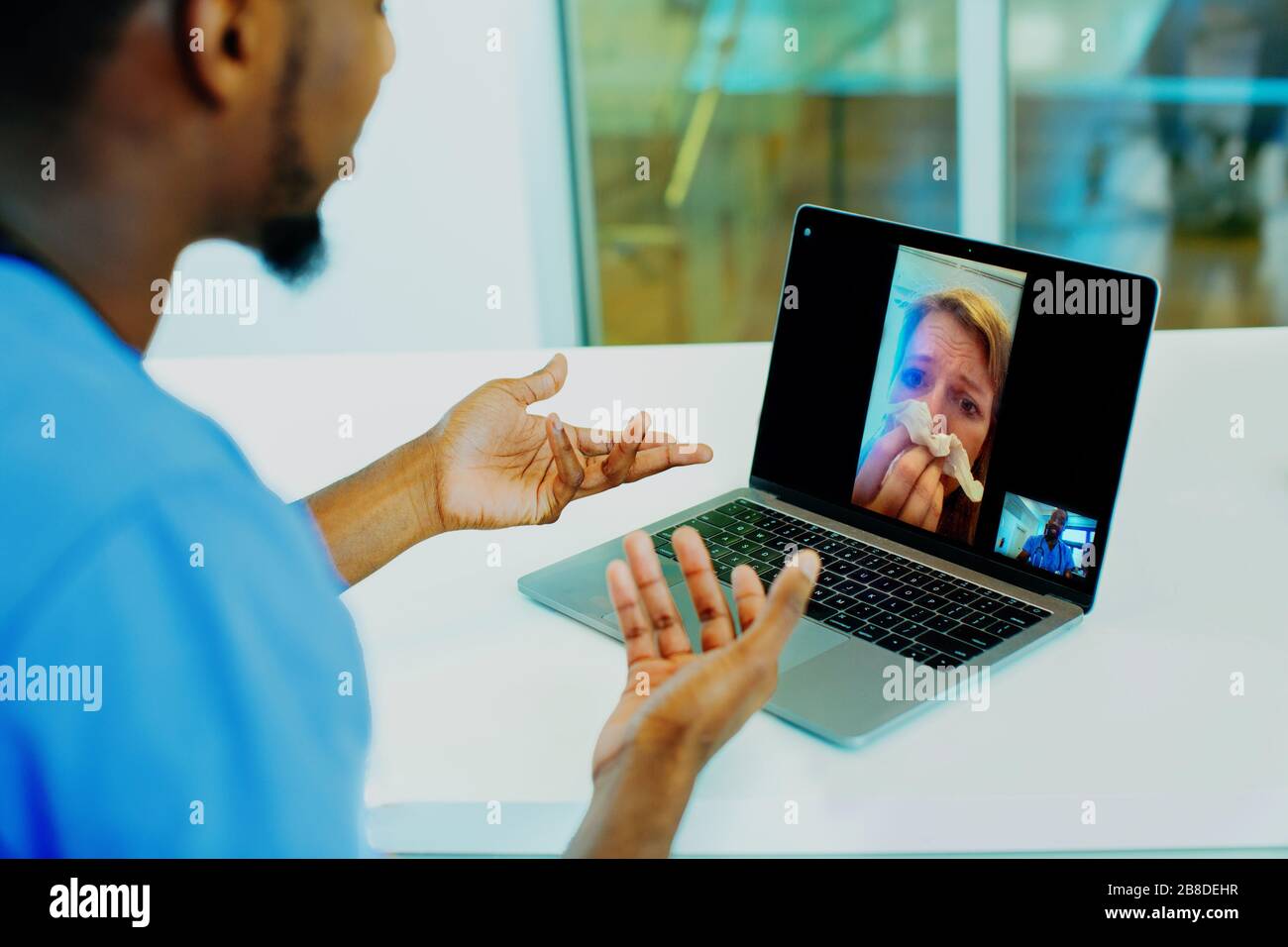 Portrait eines kranken Patienten, der über Telemedizin in Gewebe hustet und dabei von einem männlichen Arzt mit blauer Schrubbbbs-Uniform mit Laptop unterstützt wird Stockfoto