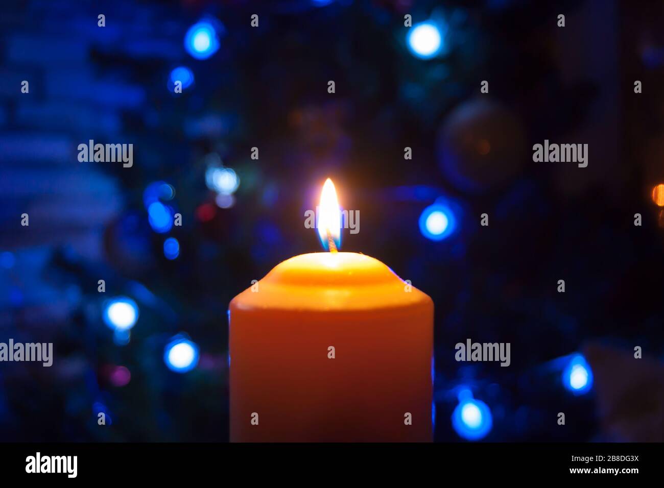 Eine große Kerze brennt vor dem Hintergrund einer Girlande mit strahlendem Licht. Vertikales Foto, Unschärfe. Mystische esoterische Romantik Divination Stimmung getauft Weihnachts-Karol-Setcer Stockfoto