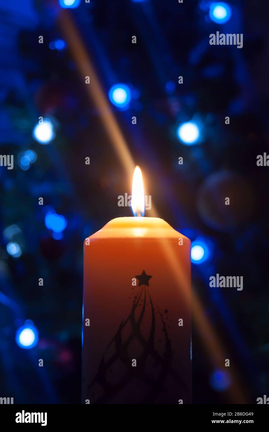Eine große Kerze brennt vor dem Hintergrund einer Girlande mit strahlendem Licht. Vertikales Foto, Unschärfe. Mystische esoterische Romantik Divination Stimmung getauft Weihnachts-Karol-Setcer Stockfoto
