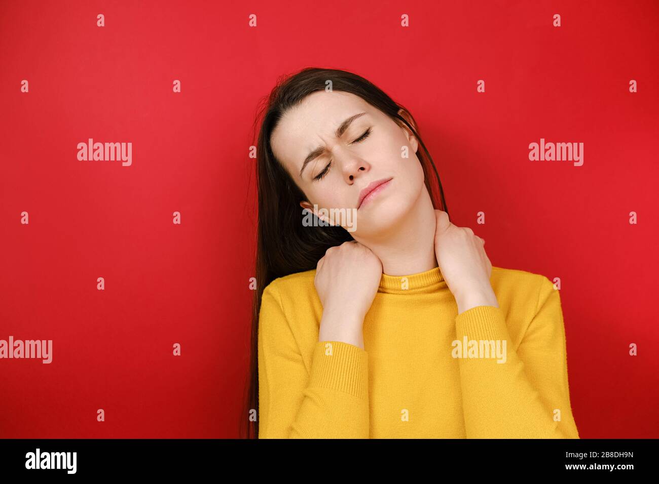 Verärgerte junge Frau, die steife Schmerzen im Nacken Konzept reiben massagewesene Muskeln leiden unter Fibromyalgie, hat düsteren Ausdruck, isoliert auf r Stockfoto