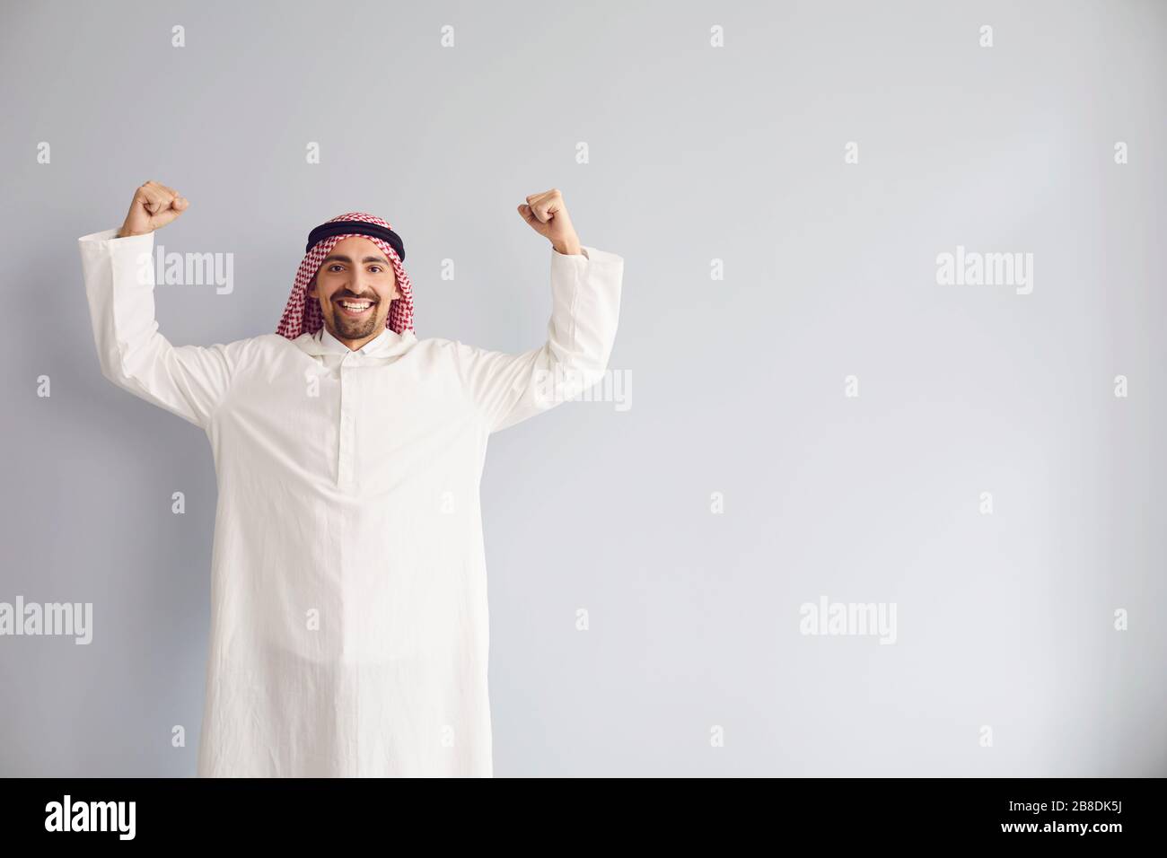 Der arabische männliche Geschäftsmann hob seine Hände lächelnd auf einem grauen Hintergrund Stockfoto