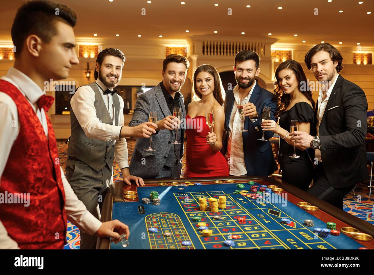 Fröhliche Freunde mit Sektgläsern, die lächeln, während sie Casino-Poker-Roulette spielen. Stockfoto