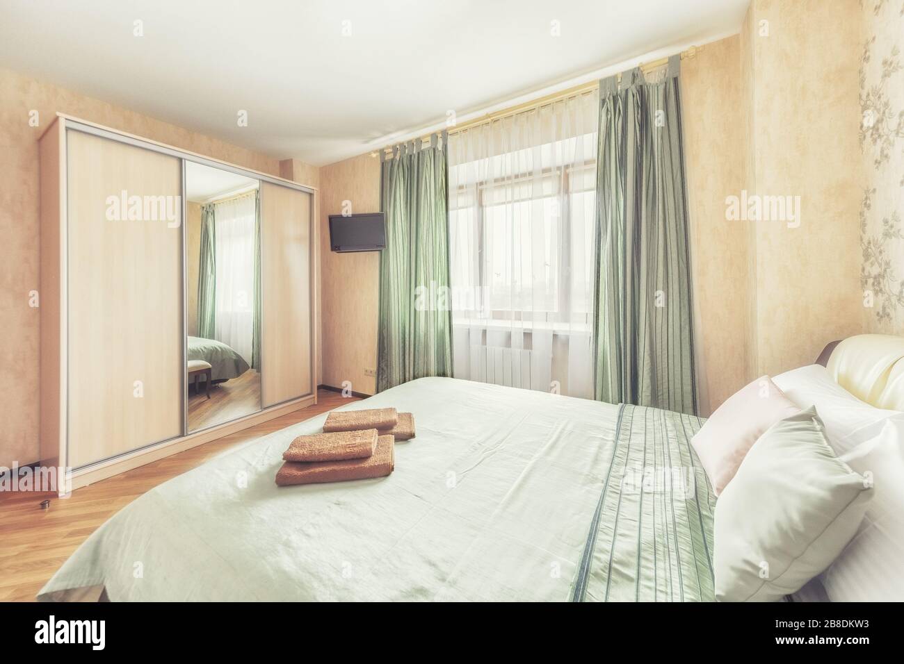 Gemütliches helles Schlafzimmer mit schrank und Fenster einfache beige Einrichtung mit grünen Betten Stockfoto