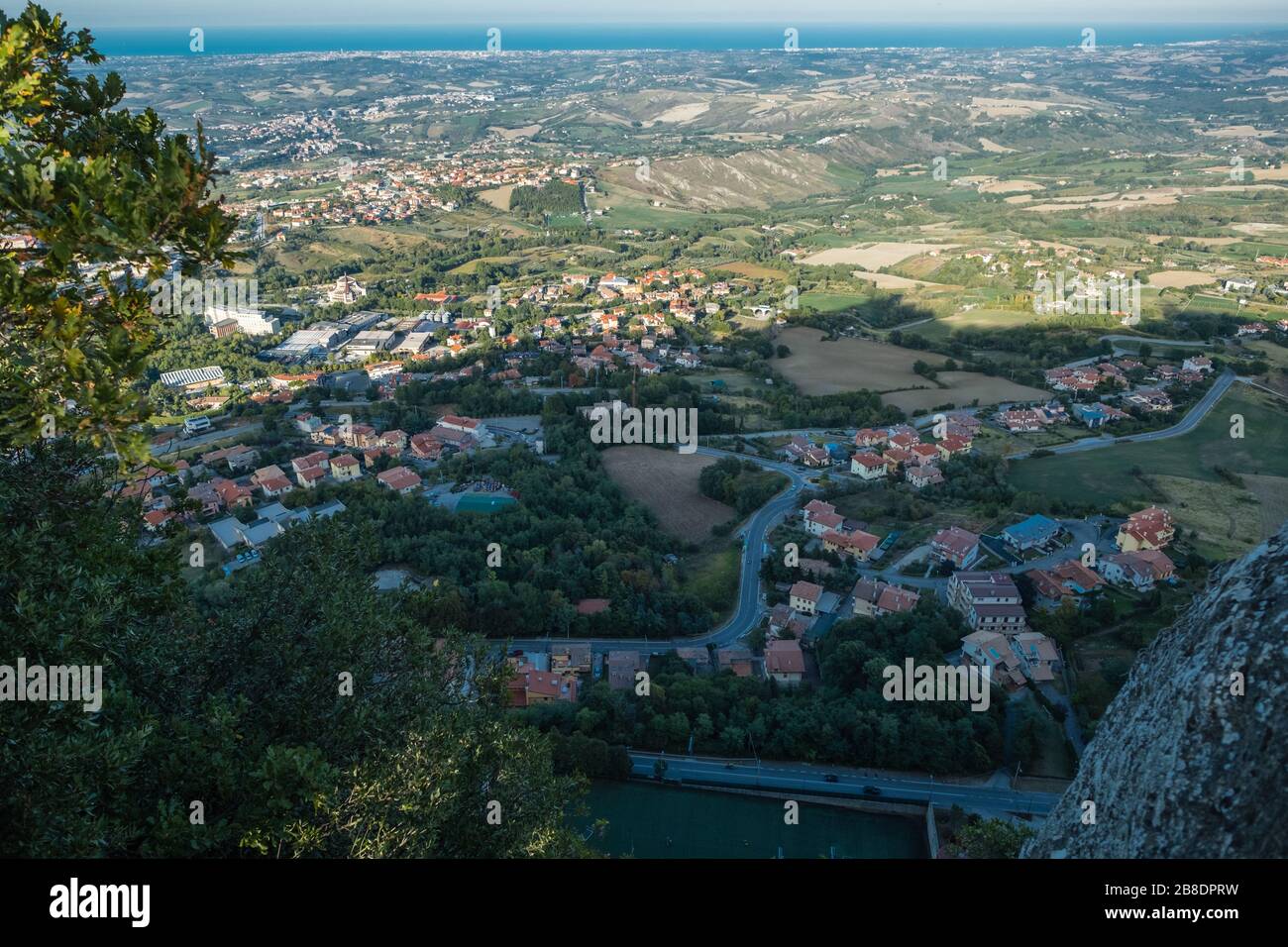 Nach unten schauen. Blick von der Festung San Marino hoch auf dem steilen Berg zu Wohngebieten unterhalb und jenseits von Italien und der Adria Stockfoto