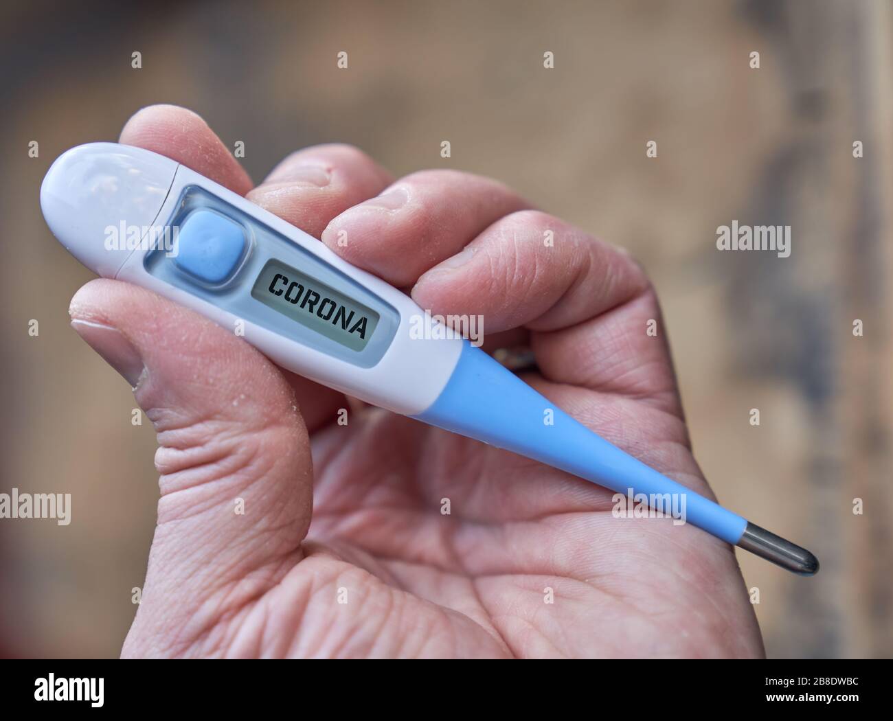 Die männliche Hand hält klinisches Thermometer mit Koronatext auf dem Bildschirm während der globalen Kovid-19- oder Corona-Pandemie Stockfoto