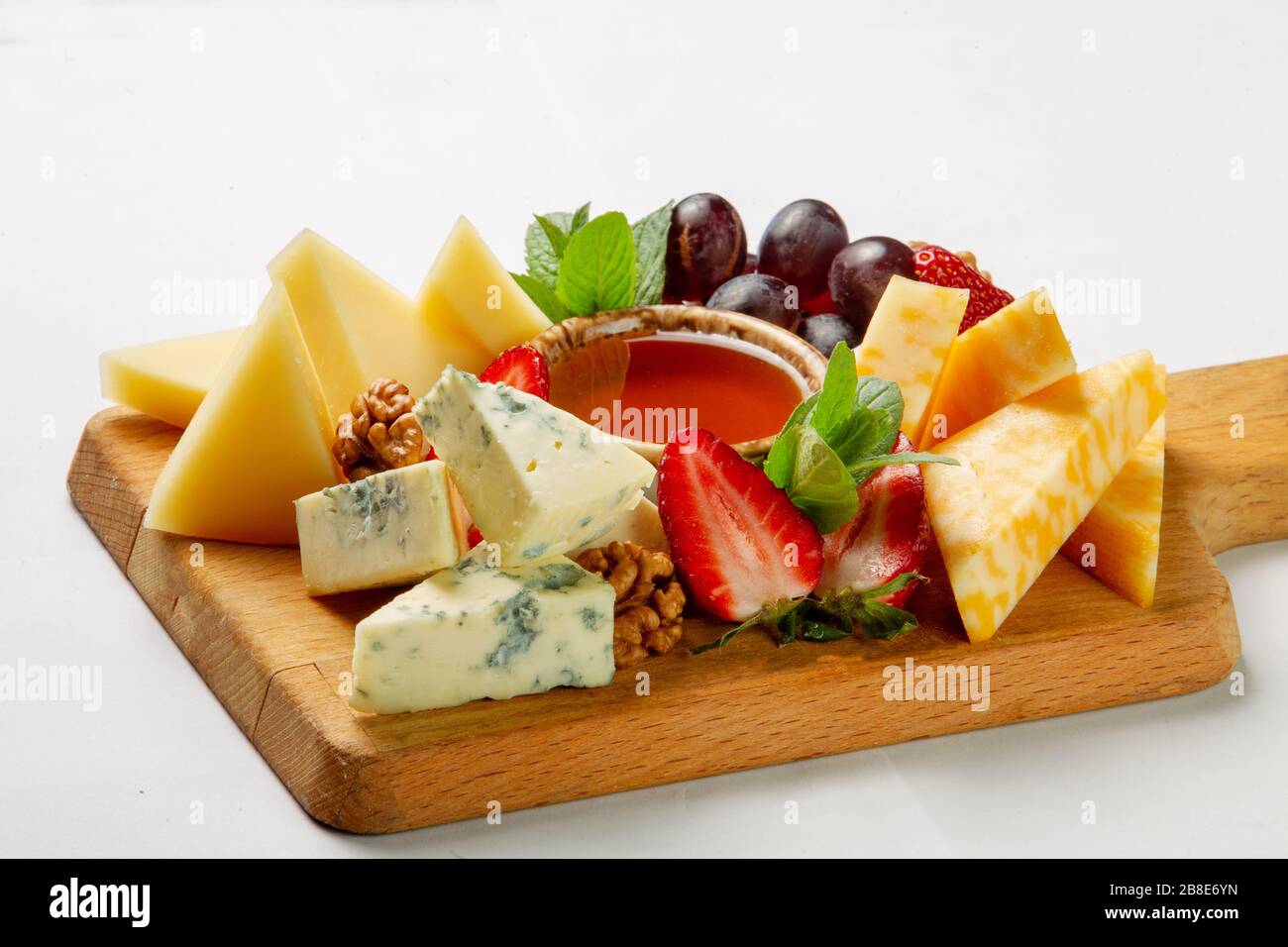 Zu den verschiedenen Käsesorten und Früchten auf dem Holztisch gehören Blaukäse und gepresster, ungekochter Käse sowie Honig und Walnüsse Stockfoto