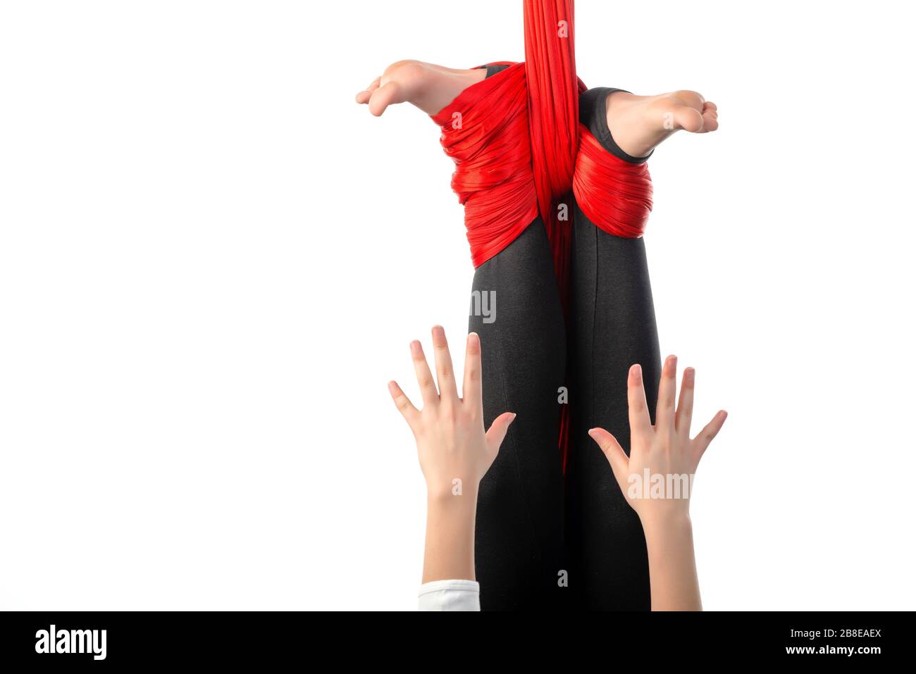 Nahaufnahme der Beine eines kleinen Mädchens, die in einem Knoten aus roten, luftigen Bändern auf weißem Grund gefesselt sind. Konzept der Luftakrobatik und sportlichen Leistungen. Adv Stockfoto