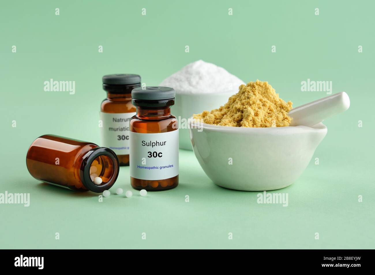 Flaschen mit Homöopathika - Schwefel, Natrum muriatikum, Substanzen und Inhaltsstoffe zur Zubereitung von Homöopathiemitteln auf grünem Hintergrund. Stockfoto