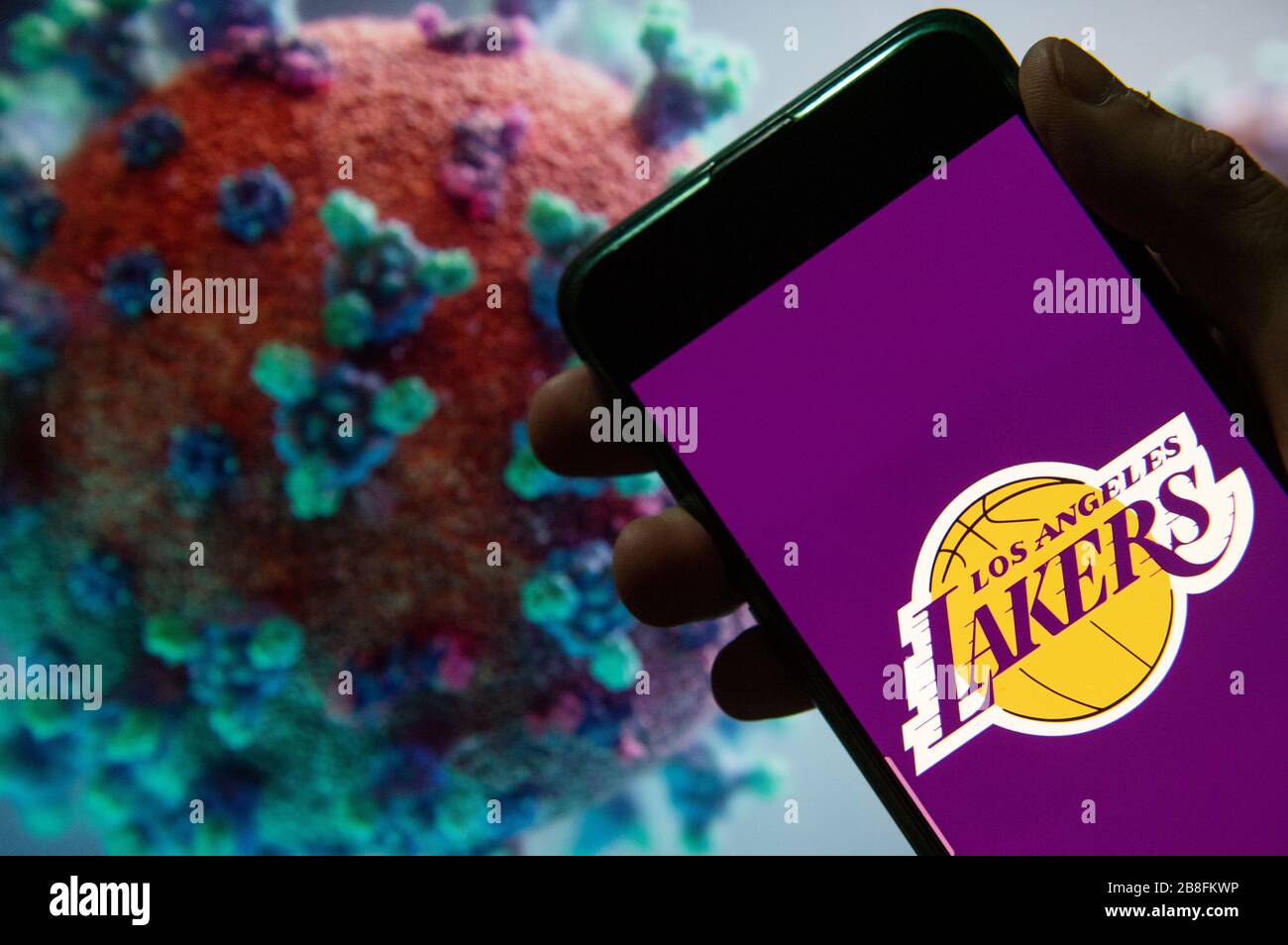 In dieser Abbildung zeigt das amerikanische Profi-Basketball-NBA-Team das Logo des Los Angeles Lakers Teams, das auf einem Smartphone mit einem Computermodell des COVID-19-Coronavirus im Hintergrund angezeigt wird. Stockfoto