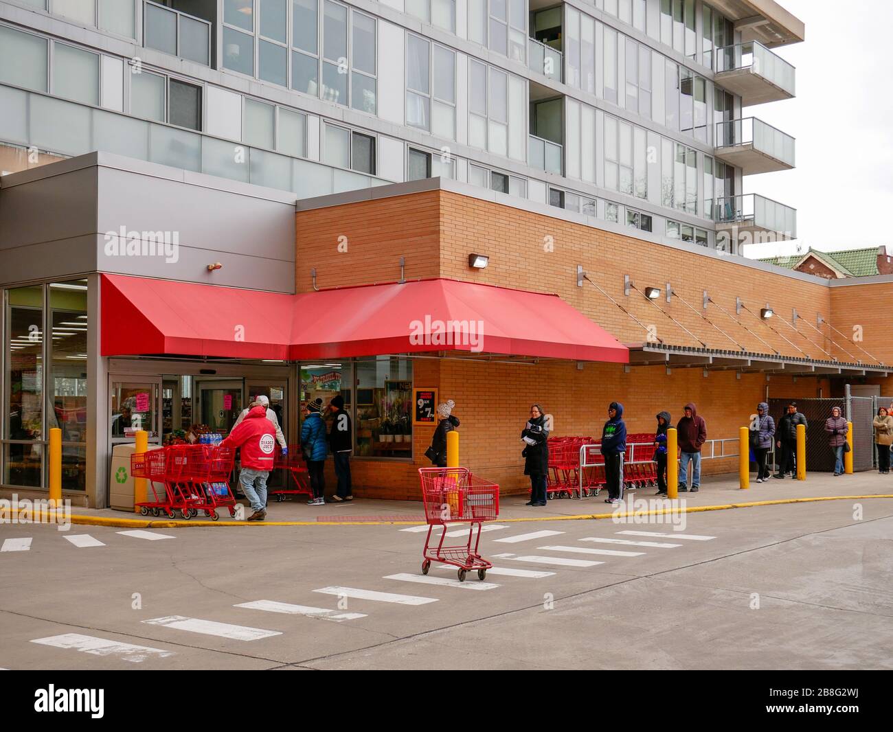 Oak Park, Illinois, USA. März 2020. Einkäufer legen sich außerhalb eines Lebensmittelgeschäftes von Trader Joe an und halten Abstand zwischen ihnen als präventive Maßnahme gegen die Verbreitung von COVID-19. Gouverneur Pritzker hat einen "Helter in Kraft"-Befehl implementiert, der heute um 17 Uhr Ortszeit in Kraft treten soll. Stockfoto