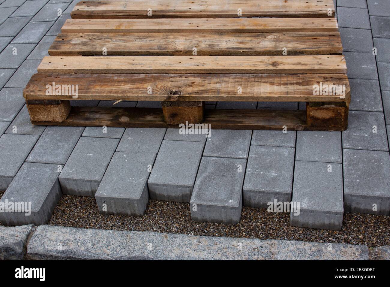 Betonfertigerblöcke, die neben einem Gebäude verlegt wurden und dem Bordstein Platz lassen, auf dem neuen Gehweg liegt eine leere Holzpalette Stockfoto
