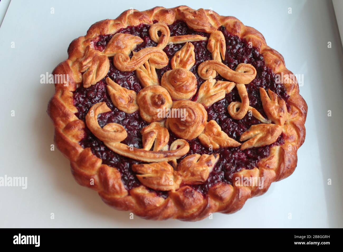 Köstlicher goldener runder Kuchen mit roter Kirsche und Lingonbeere, die mit Teigmuster auf weißem Hintergrund gefüllt sind. Stockfoto