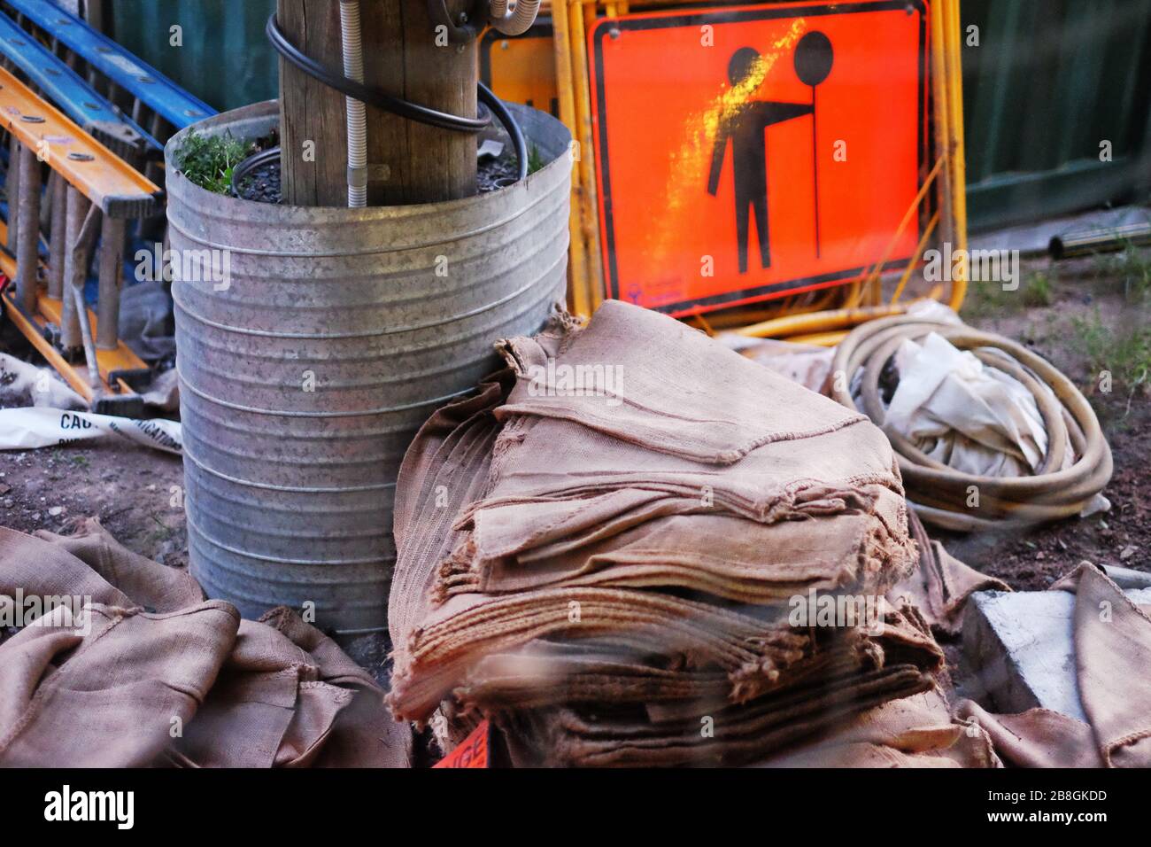 Außenbaustelle mit einem Stapel von hessischen Taschen, Leitern, einem orangefarbenen Pop-Mann-Schild, einem Pfosten im Fass, Bauarbeiten in Sydney, Australien Stockfoto