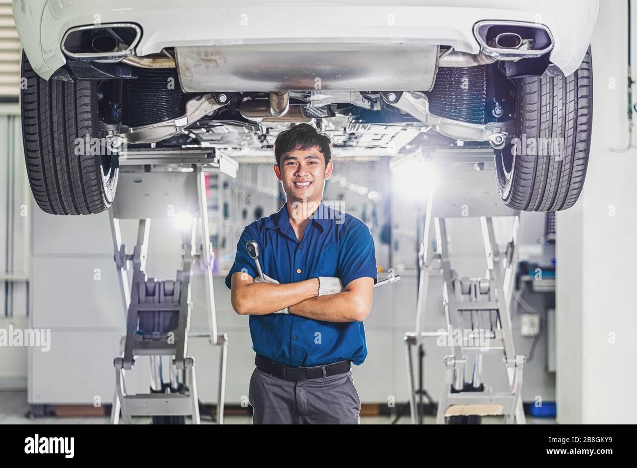Portrait asiatischer Mechaniker mit Reparaturausrüstung unter dem Auto im Wartungszentrum, das Teil des Ausstellungsraums, Techniker oder Engi ist Stockfoto