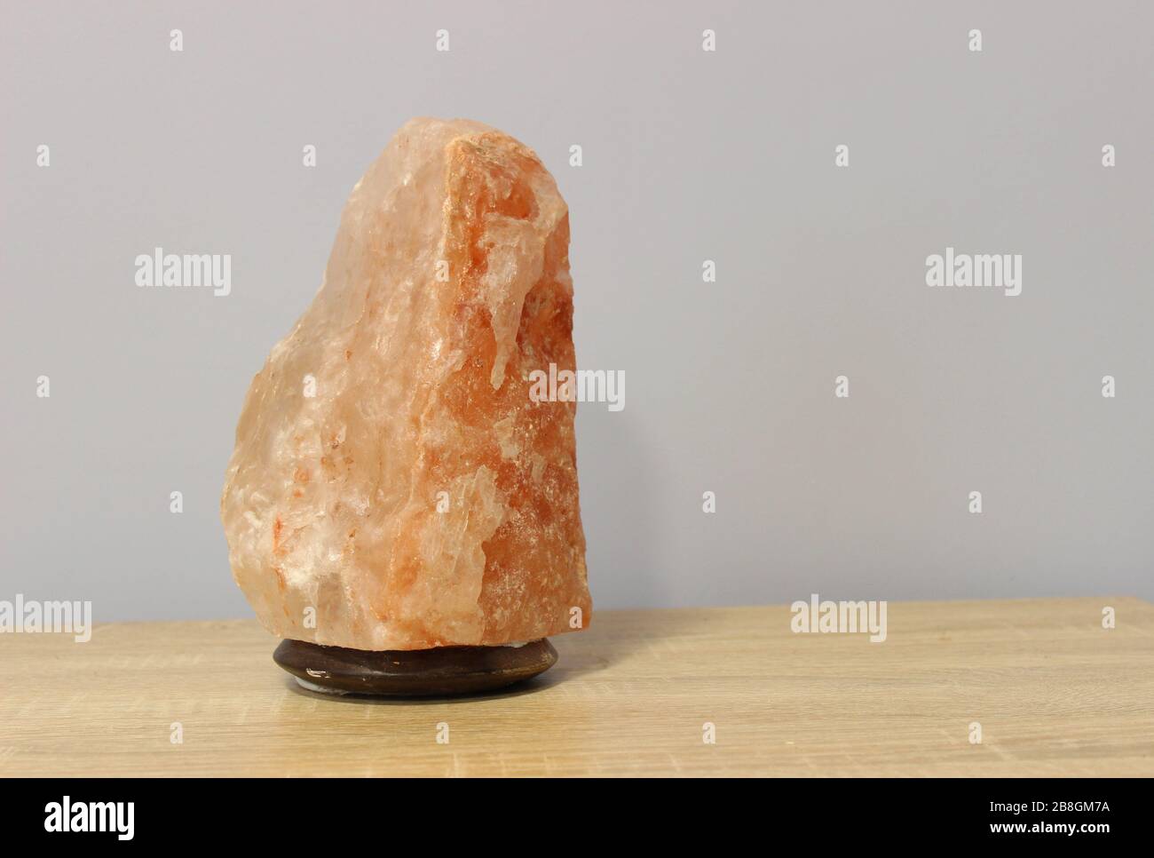 Ausgeschaltet wurde eine rosafarbene Salzlampe aus dem Himalaya, die in Form eines Felsens auf einem hellen Tisch gehauen wurde. Stockfoto