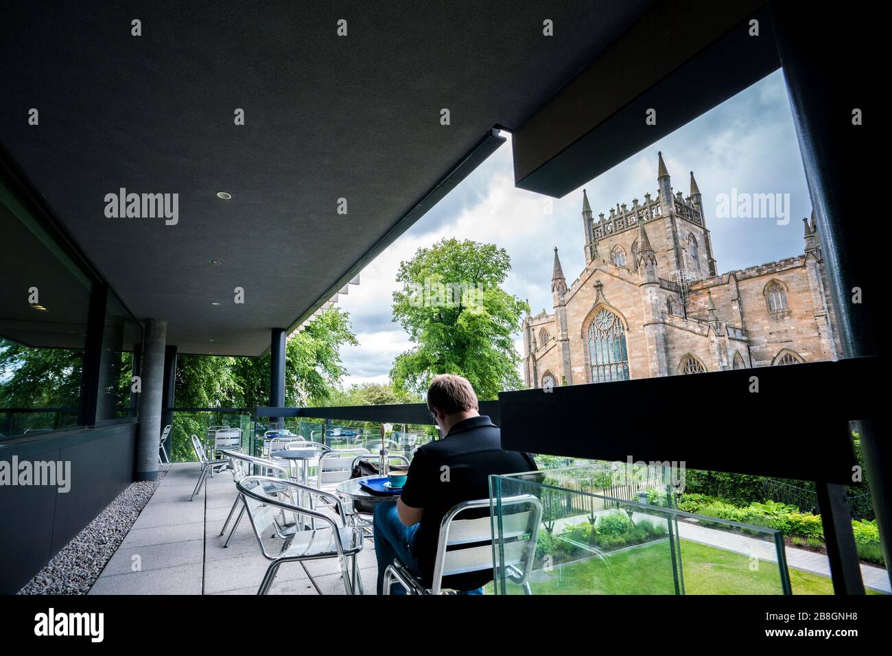 Der Mann genießt Kaffee und einen Scone im Freien mit Blick auf Dunfermline Abbey, eine Church of Scotland Parish Church, von einem Bäcker-Café, Dunfermline; Kingdom of Stockfoto