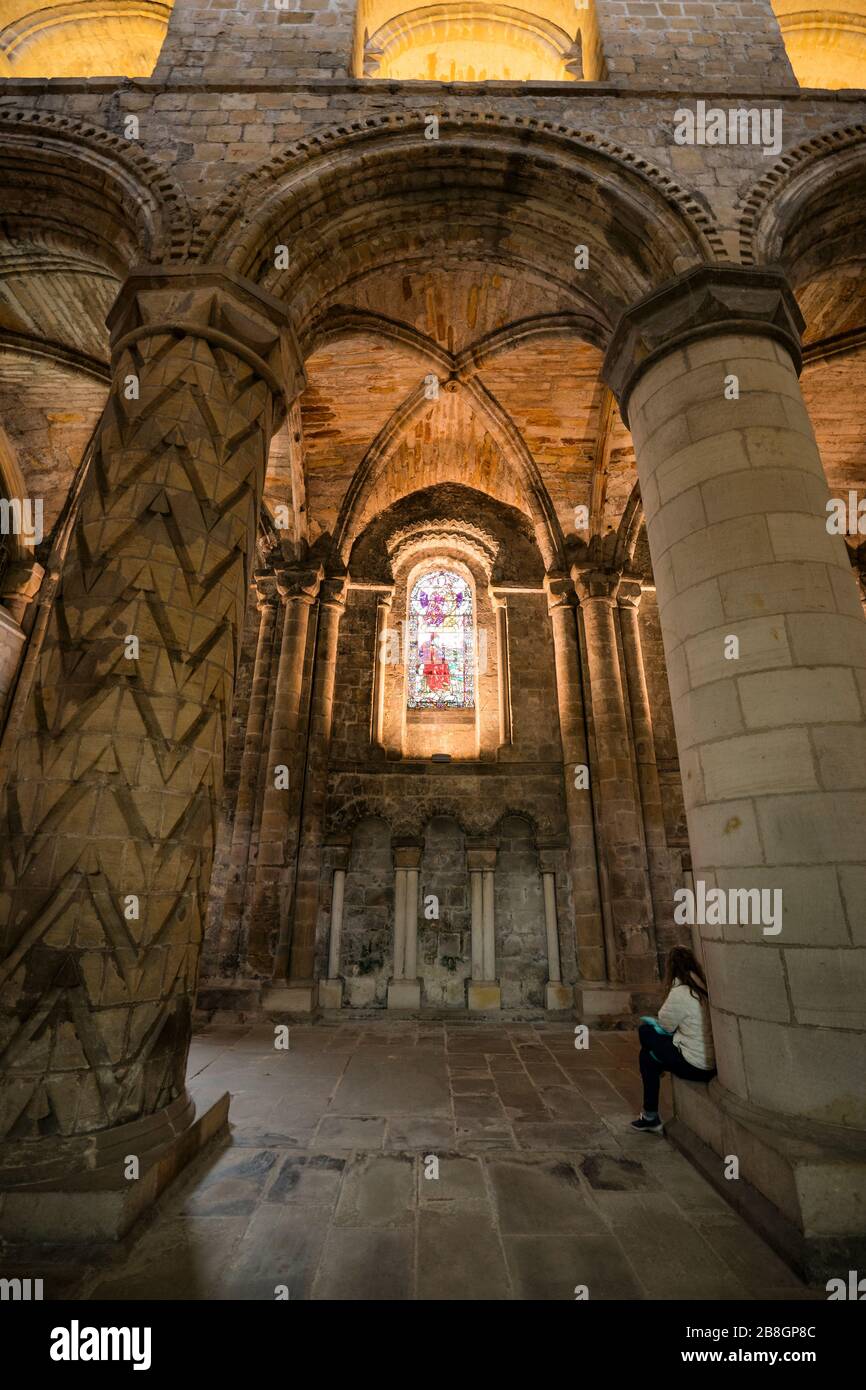 Weibliche Touristin sitzt auf der Basis einer geschnitzten Säule, die die Glasmalerei in Dunfermline Abbey, einer Church of Scotland Parish Church, Dunfermline, bewundert; Stockfoto