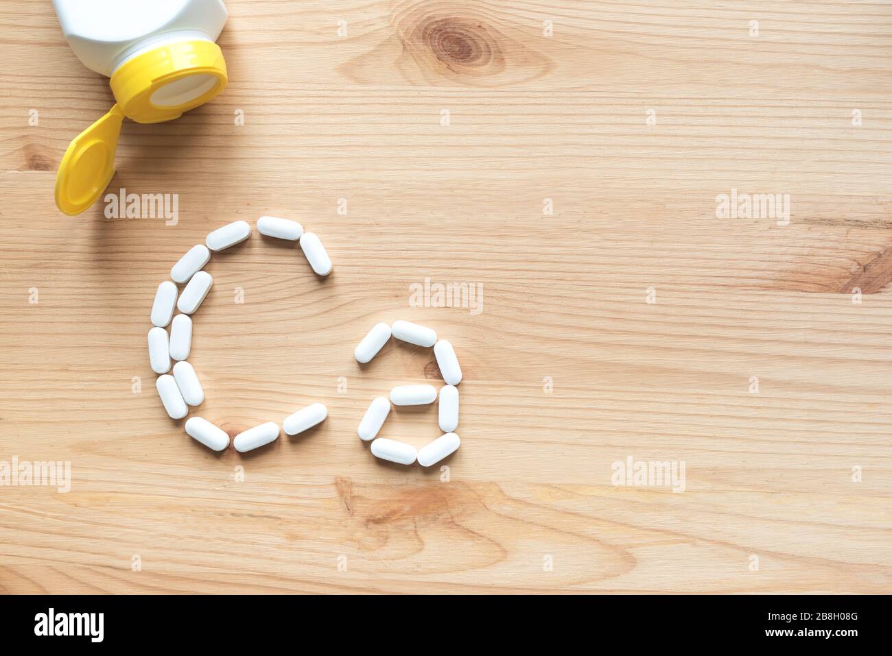 Kalziumtabletten. Weiße Pillen, die sich in Form eines Ca-Alphabets auf Holzhintergrund bilden, Kopierraum, Draufsicht. Stockfoto