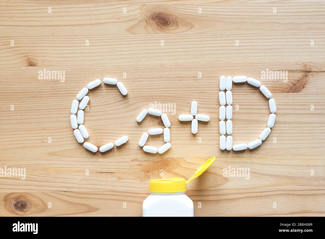 Kalzium und Vitamin D Generische Tabletten. Weiße Pillen, die Form des CA+D-Alphabets auf Holzhintergrund bilden, Kopierbereich, Draufsicht. Stockfoto