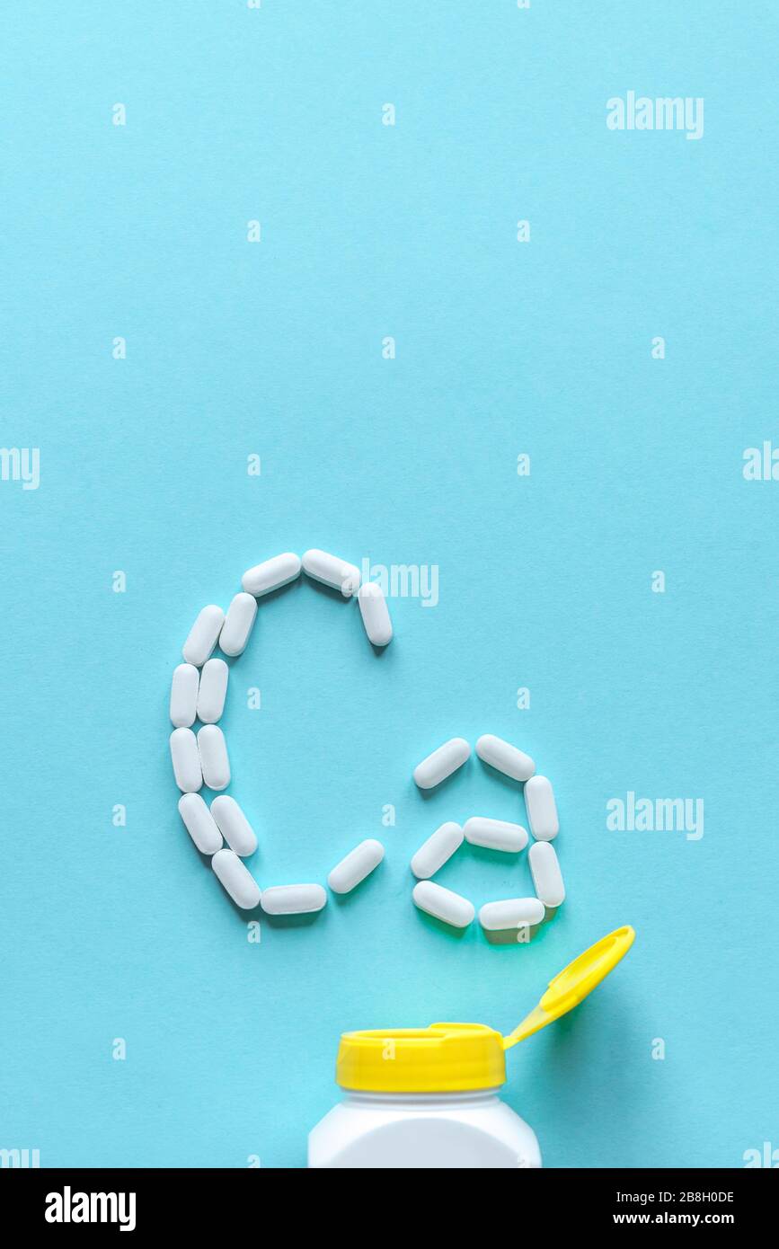 Kalziumpillen. Weiße Tabletts, die sich auf blauem Hintergrund in Form eines Ca-Alphabets bilden, Kopierbereich, Draufsicht. Stockfoto