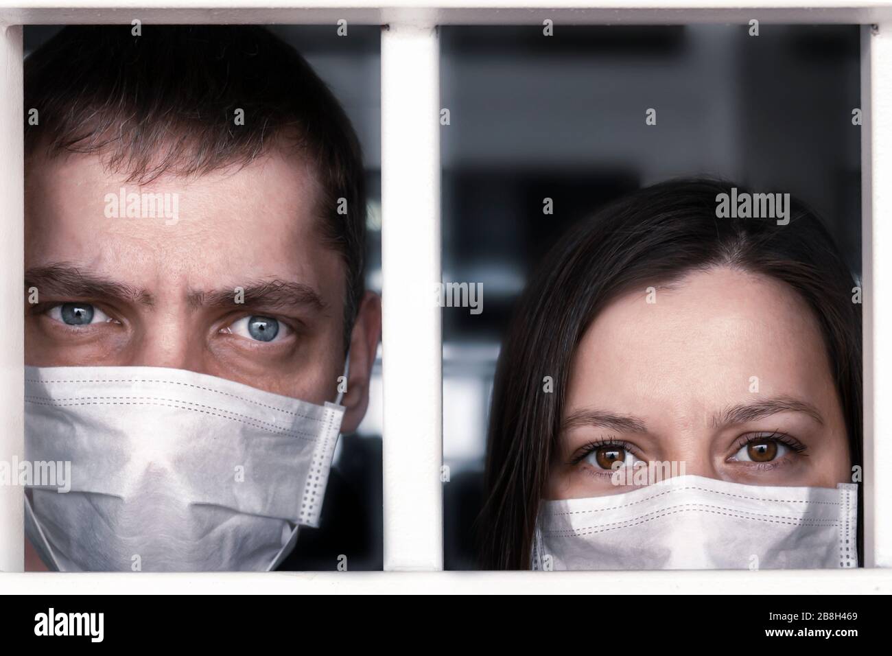 Quarantäne. Ein kranker Mann und eine Frau in schützenden medizinischen Masken blicken durch die Krankenhausbarren, Emotionen im Gesicht - Angst, Frechel und Panik. Die Ausbreitung Stockfoto