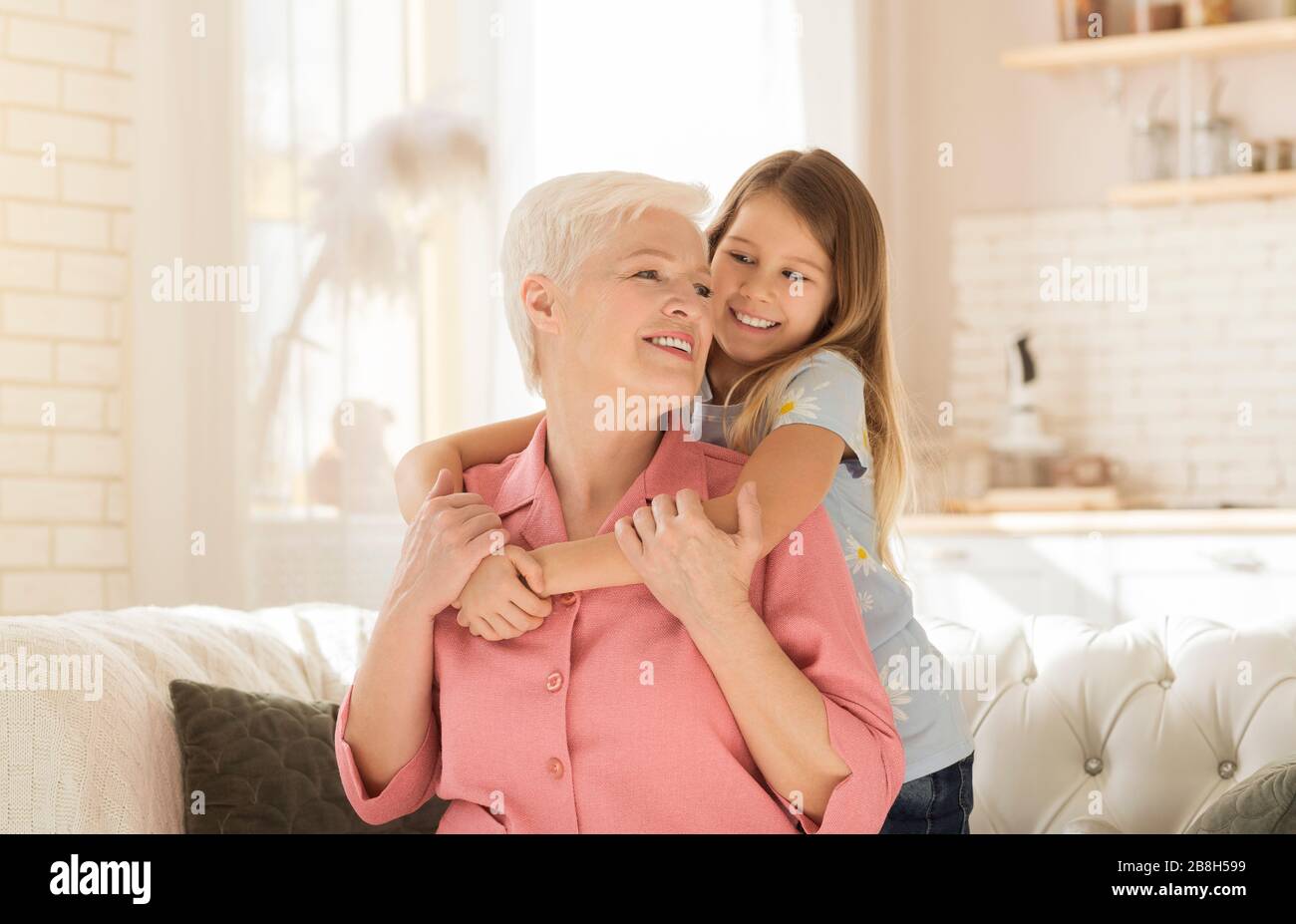 Familienbindung. Hübsches kleines Mädchen, das ihre Oma glücklich in einem hellen Wohnzimmer verkörpern kann Stockfoto