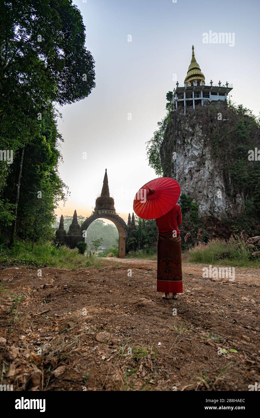 Frauen in thailändischen Nationaltrachten mit dem roten Regenschirm, der vor der Haupttür steht, der Zeit des Wartens, dem vergangenen Bild, der Zeitpforte Transla Stockfoto