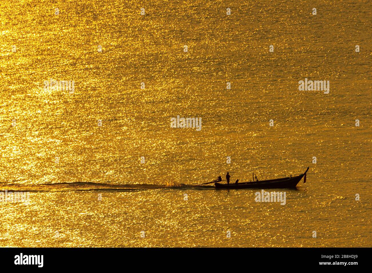 Der Sonnenuntergang, die Meeresoberfläche reflektiert das Sonnenlicht in Gold. Das Schiff lief durch die glitzernde Meeresoberfläche. Stockfoto