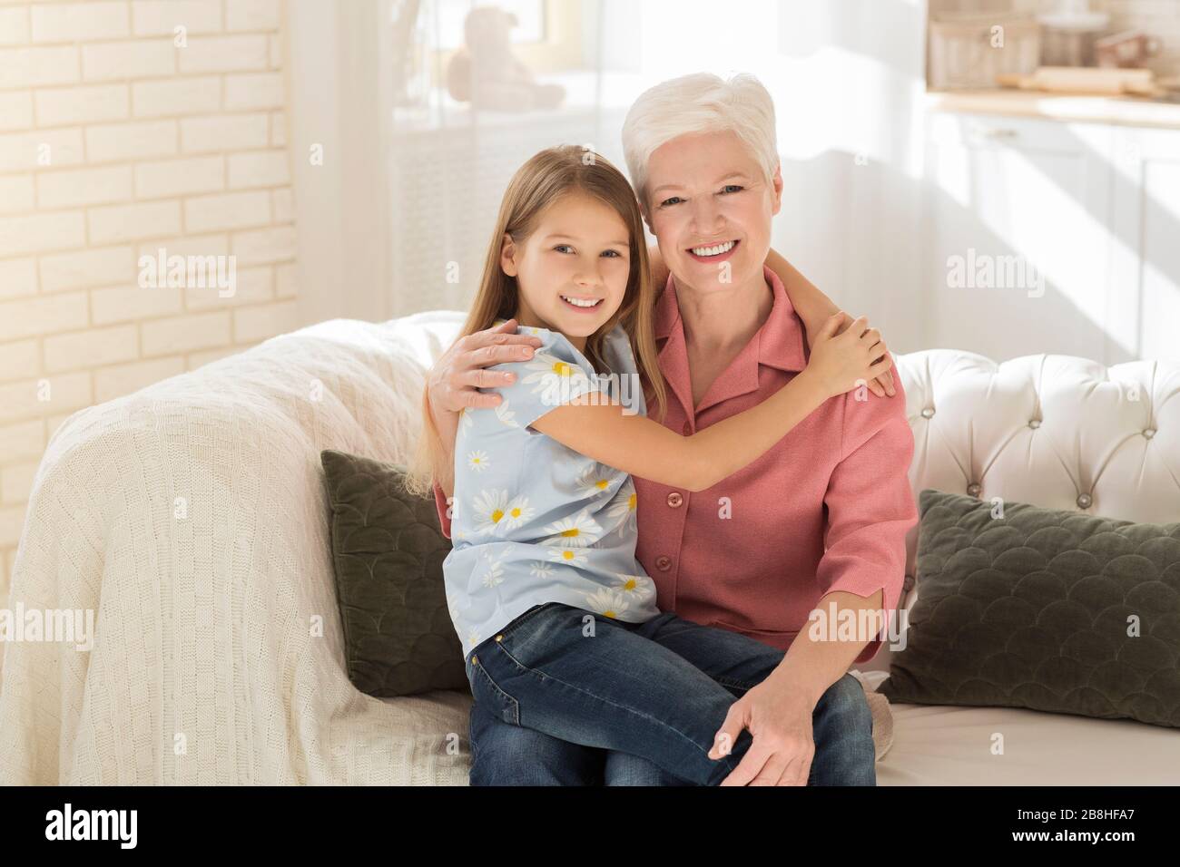 Freundschaft zwischen den Generationen. Süßes Kind mit ihrer Granny, die sich in einem sonnenbeleuchteten Zimmer umarmt Stockfoto